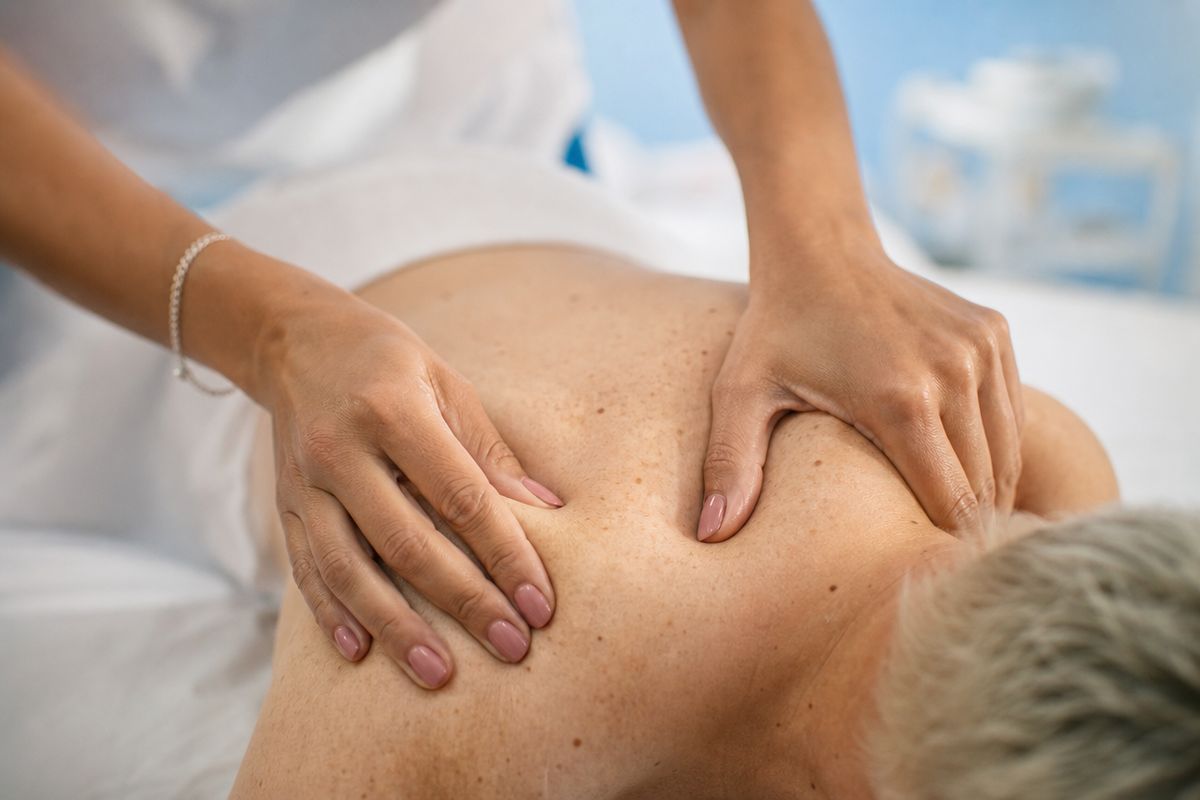 Massage therapist working both hands into a client's shoulder and upper back